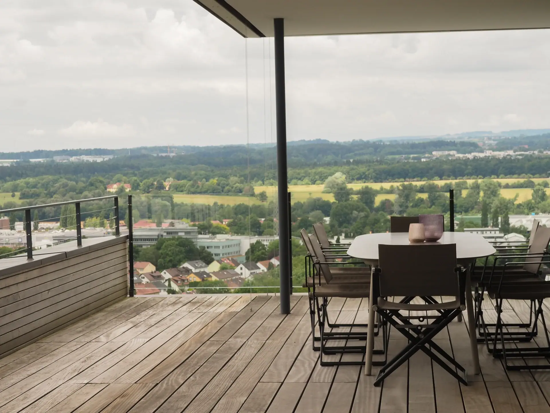 Überdachte Dachterrasse mit Esstisch und weitem Blick über Häuser und grüne Landschaft.