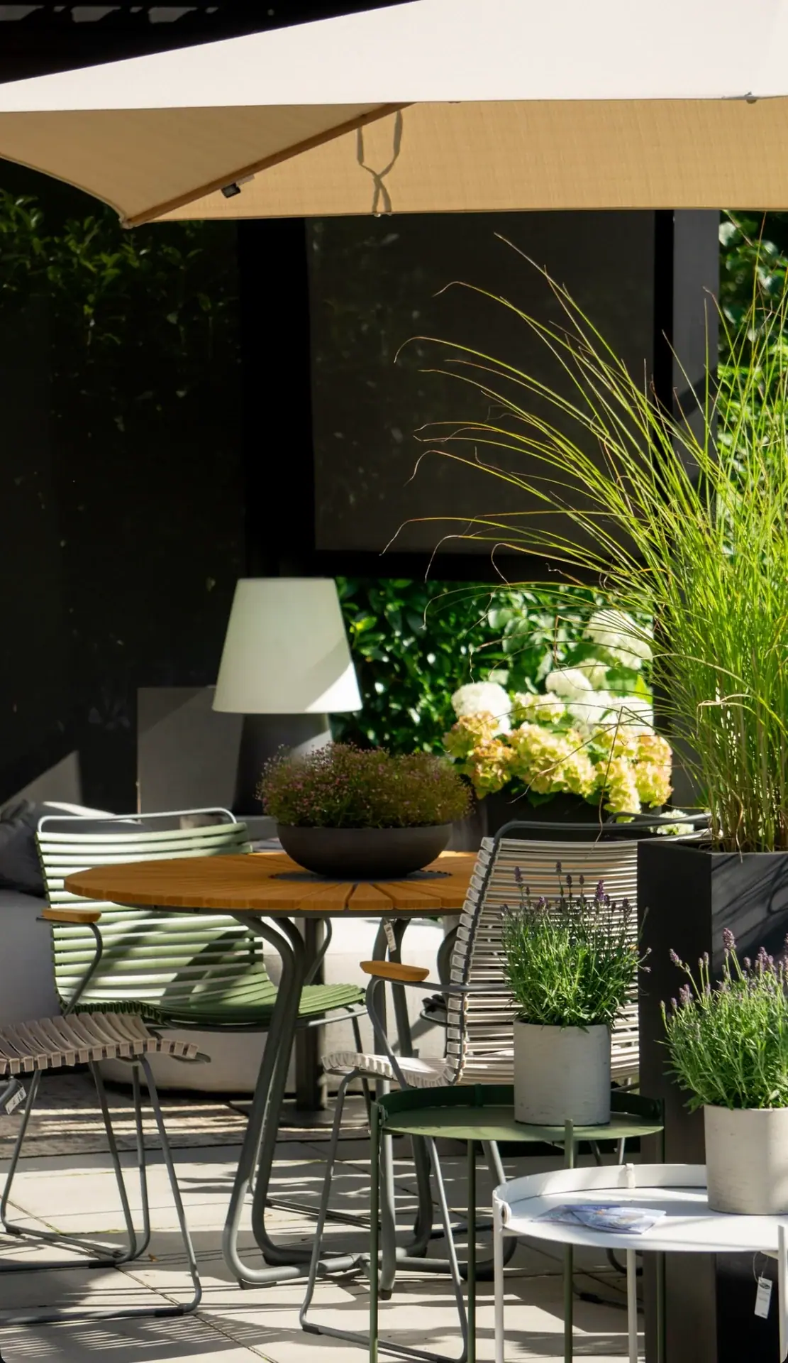 Gartensitzgruppe mit rundem Tisch, Stühlen und Pflanzgefäßen unter einer Markise.