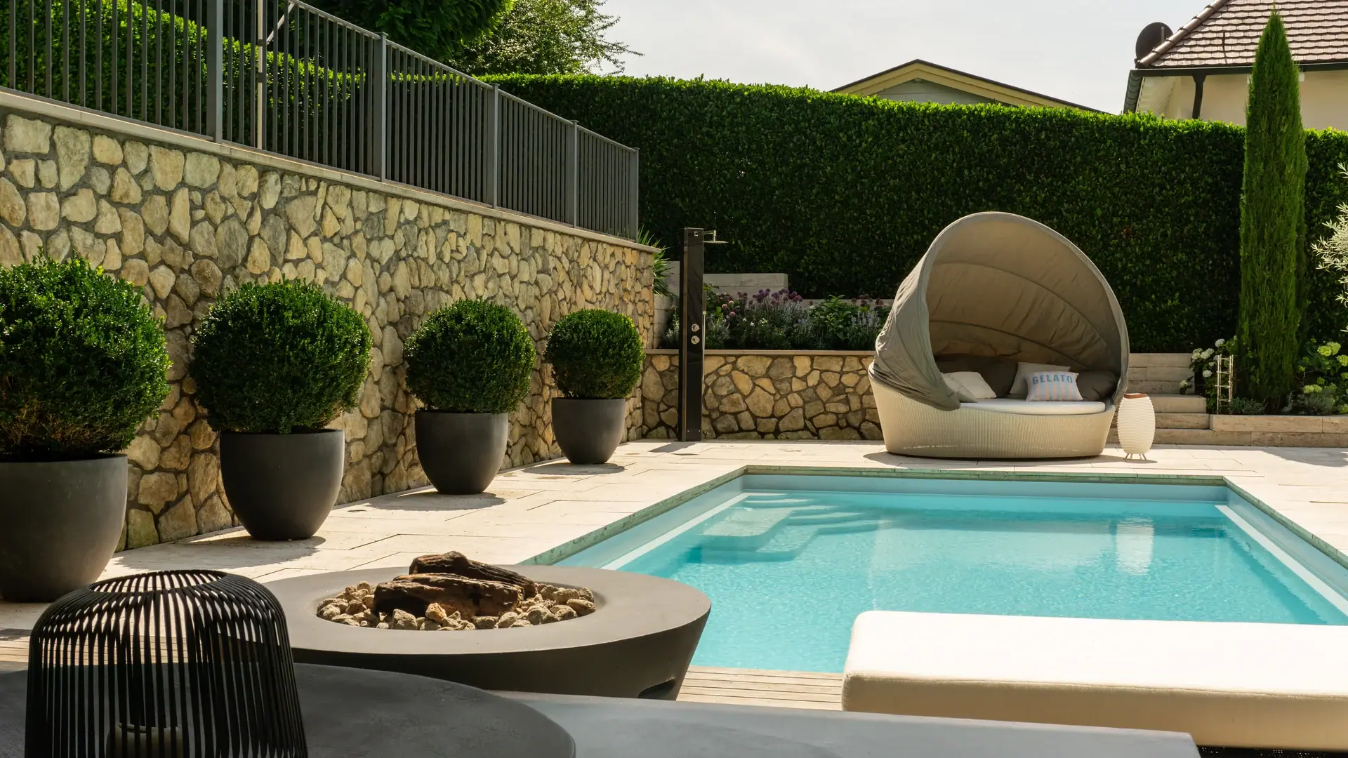 Gartengestaltung von WohnraumGarten: Pool mit Natursteinmauer, Formgehölzen und überdachter Gartenliege