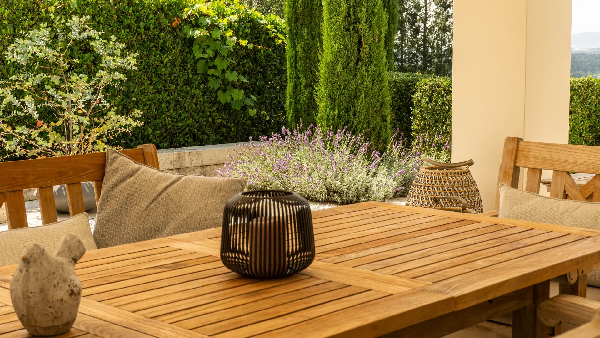 Überdachter Sitzplatz mit Teakholztisch, Gartenmöbeln und Laterne vor Lavendel und Hecke