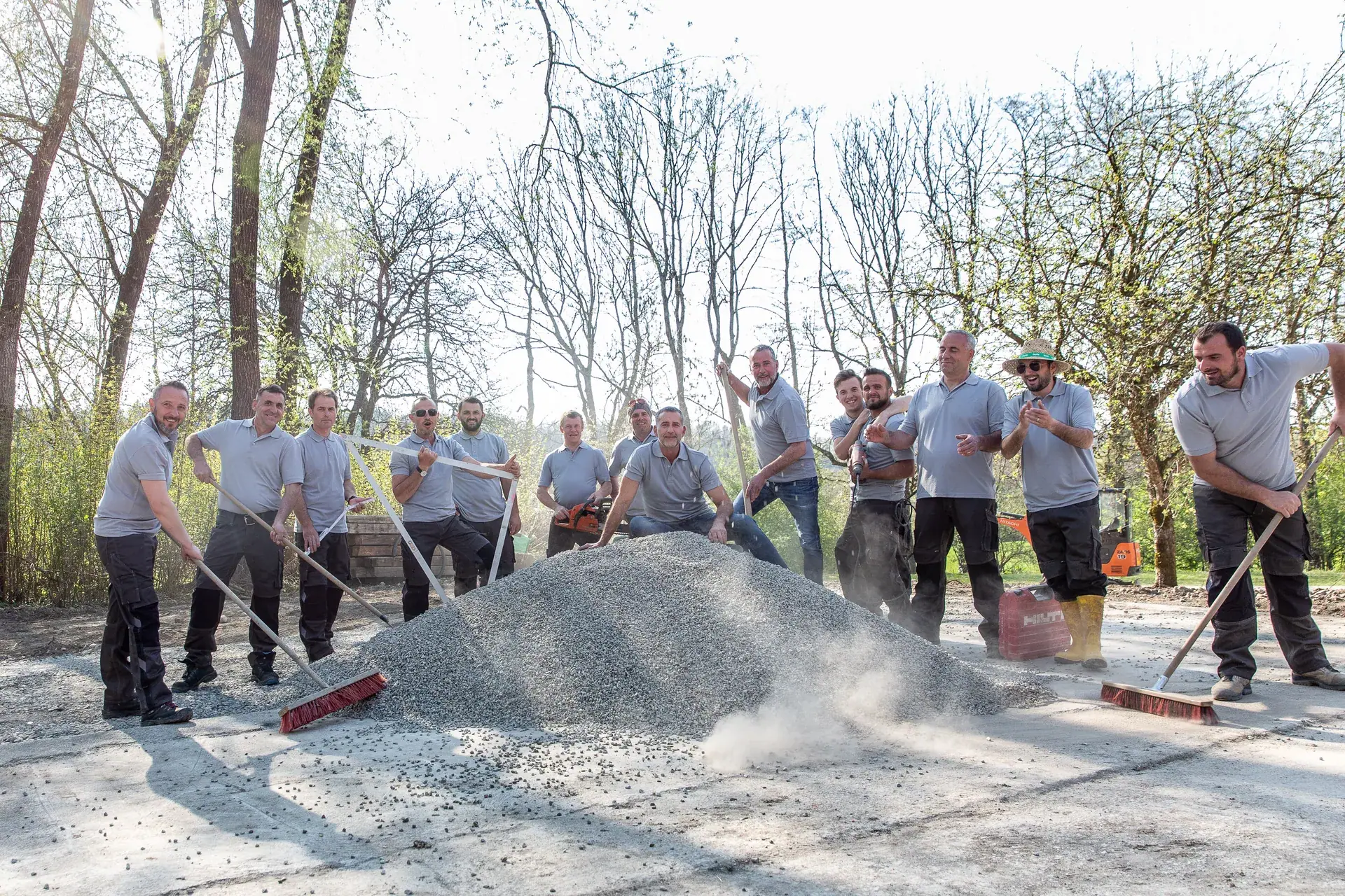 Das Team von WohnraumGarten mit Besen und Schaufeln rund um einen Kieshaufen