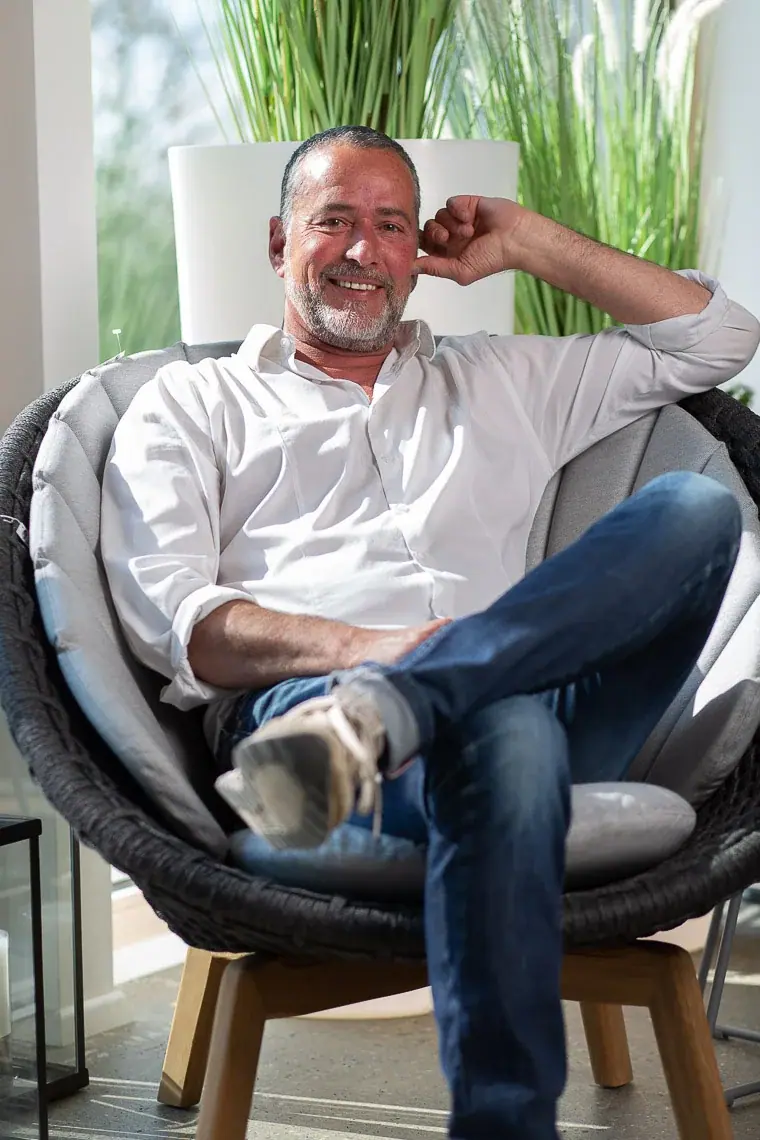 Frank Liewig, lächelnd in einem Rattansessel vor Ziergräsern