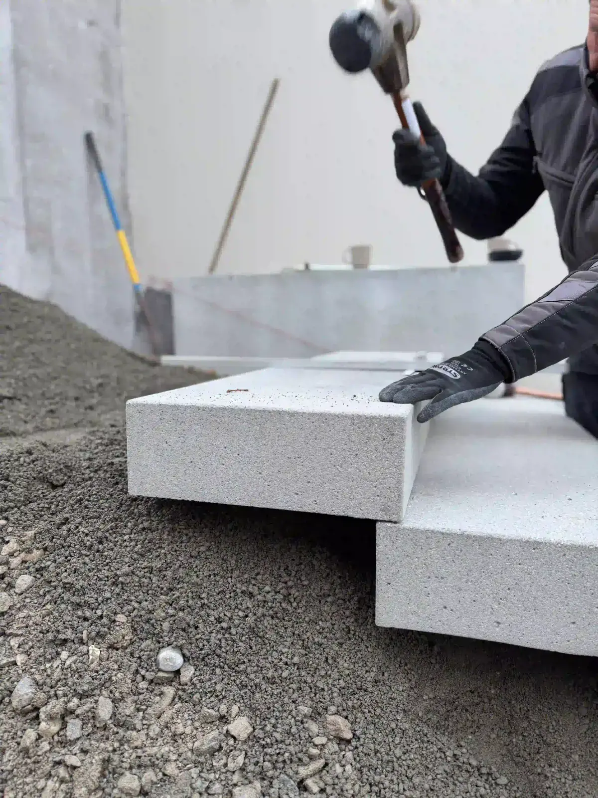 Mitarbeiter setzt mit dem Hammer helle Blockstufen auf ein Kiesbett