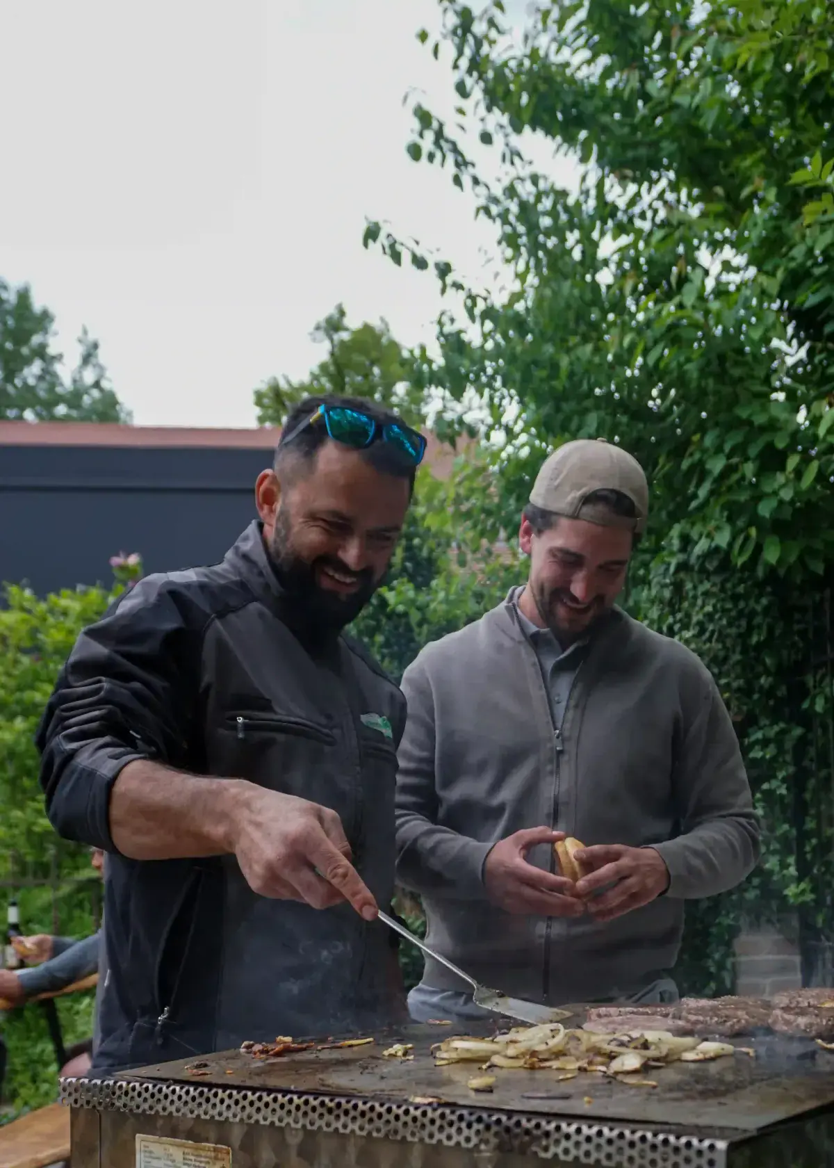 Zwei Kollegen lachen beim Grillen im Garten