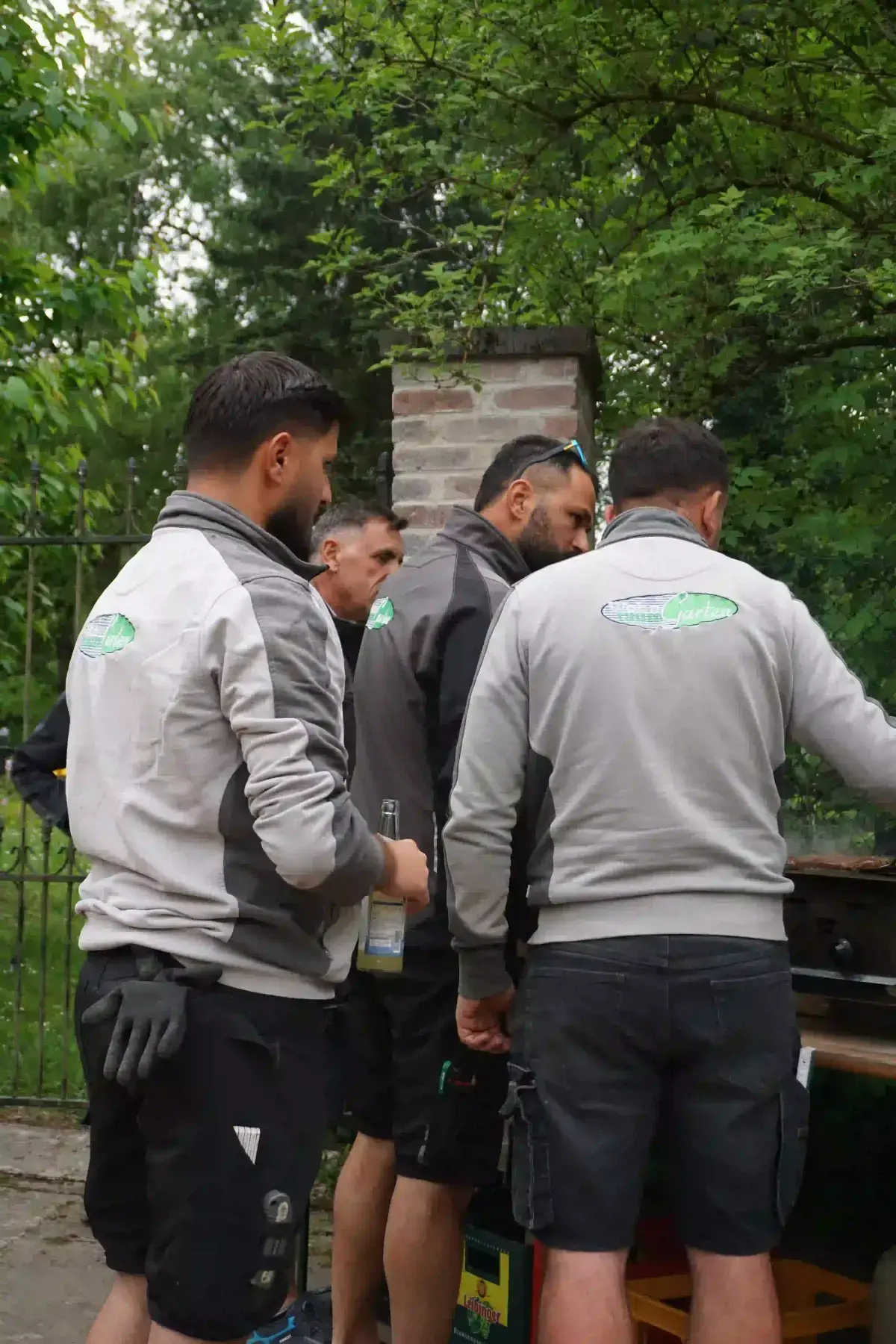 Mitarbeiter in grauen Jacken mit Firmenlogo stehen beim gemeinsamen Grillen zusammen