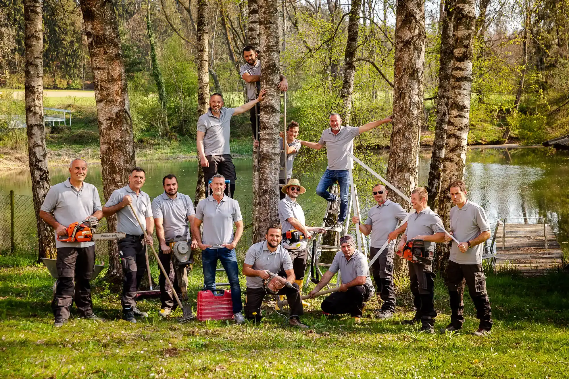 Das Team von WohnraumGarten mit Motorsägen, Spaten und Leiter zwischen Birken an einem Teich