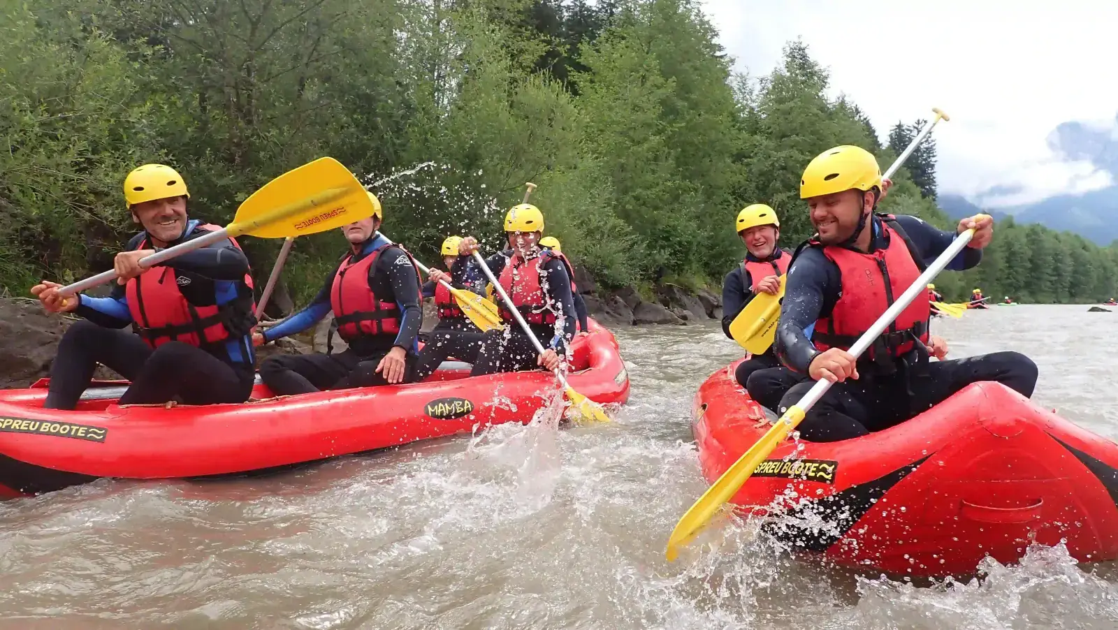 Teamevent: Kolleginnen und Kollegen paddeln mit Helmen und Schwimmwesten in roten Schlauchbooten durch einen Fluss