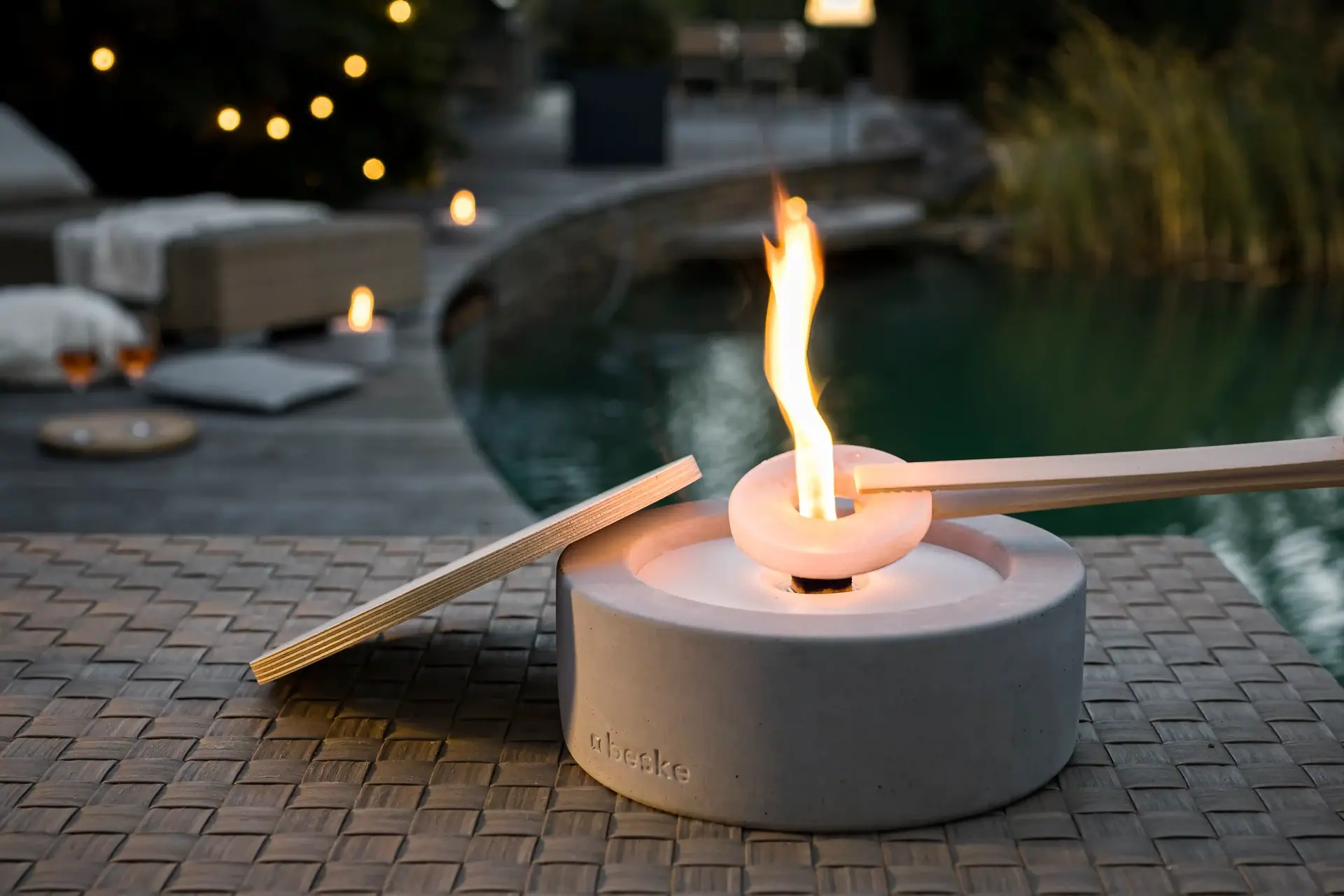 Brennendes Tischfeuer aus Beton neben einem Pool.