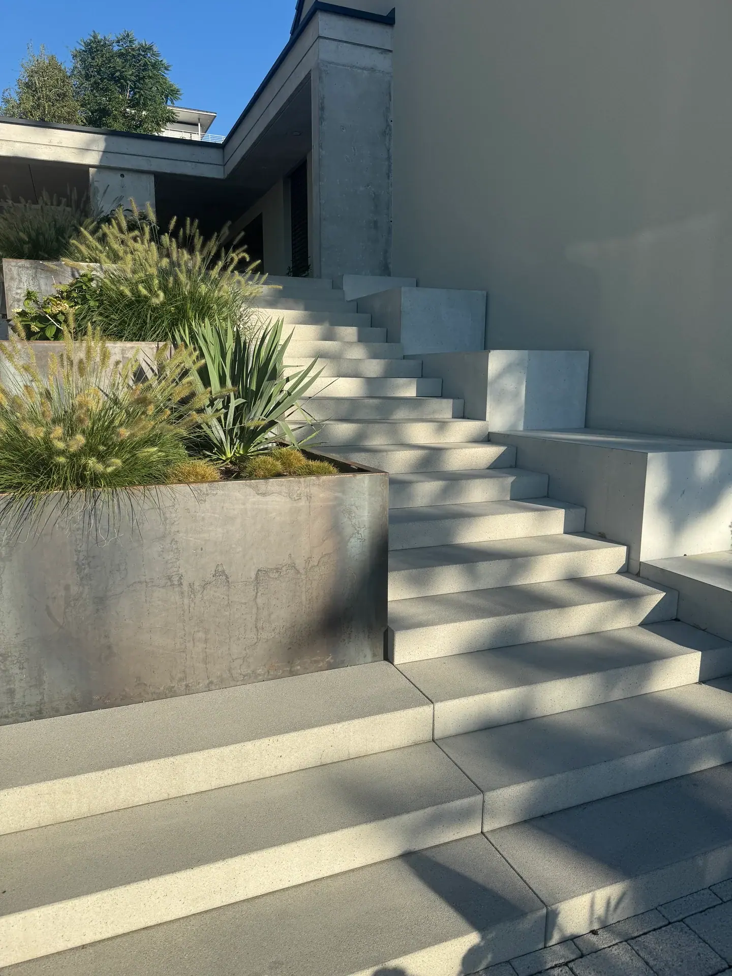 Helle Betontreppe zwischen bepflanzten Stahlbeeten.