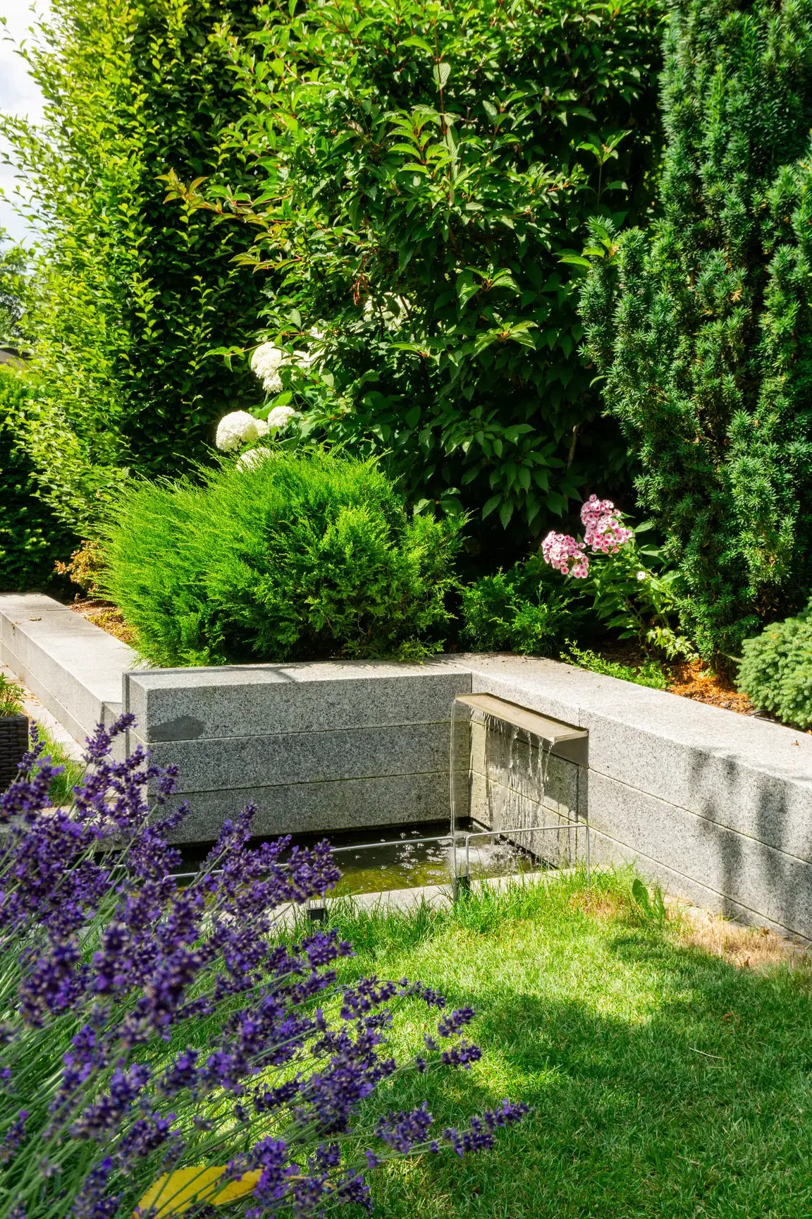 Kleines Wasserelement in einem bepflanzten Gartenbeet.