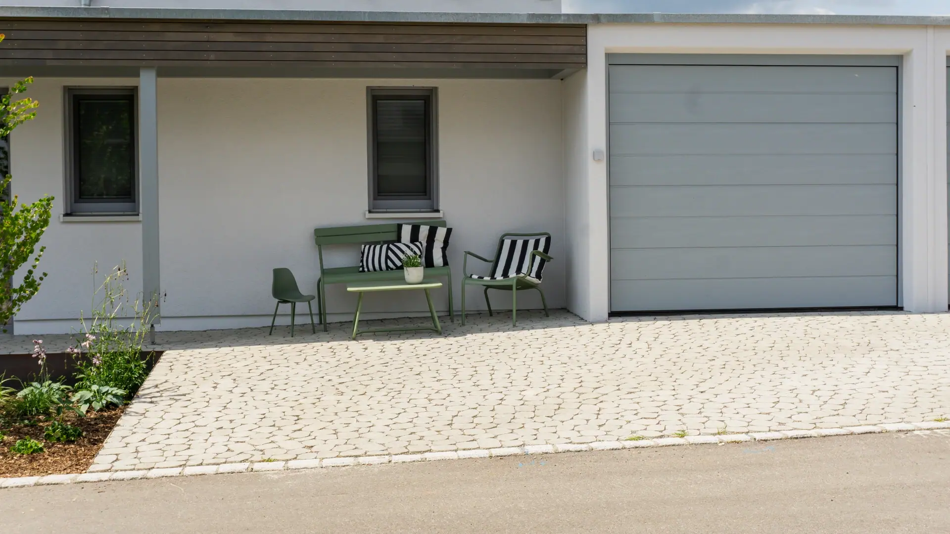 Gepflasterte Einfahrt vor einer Garage mit kleiner Sitzbank.