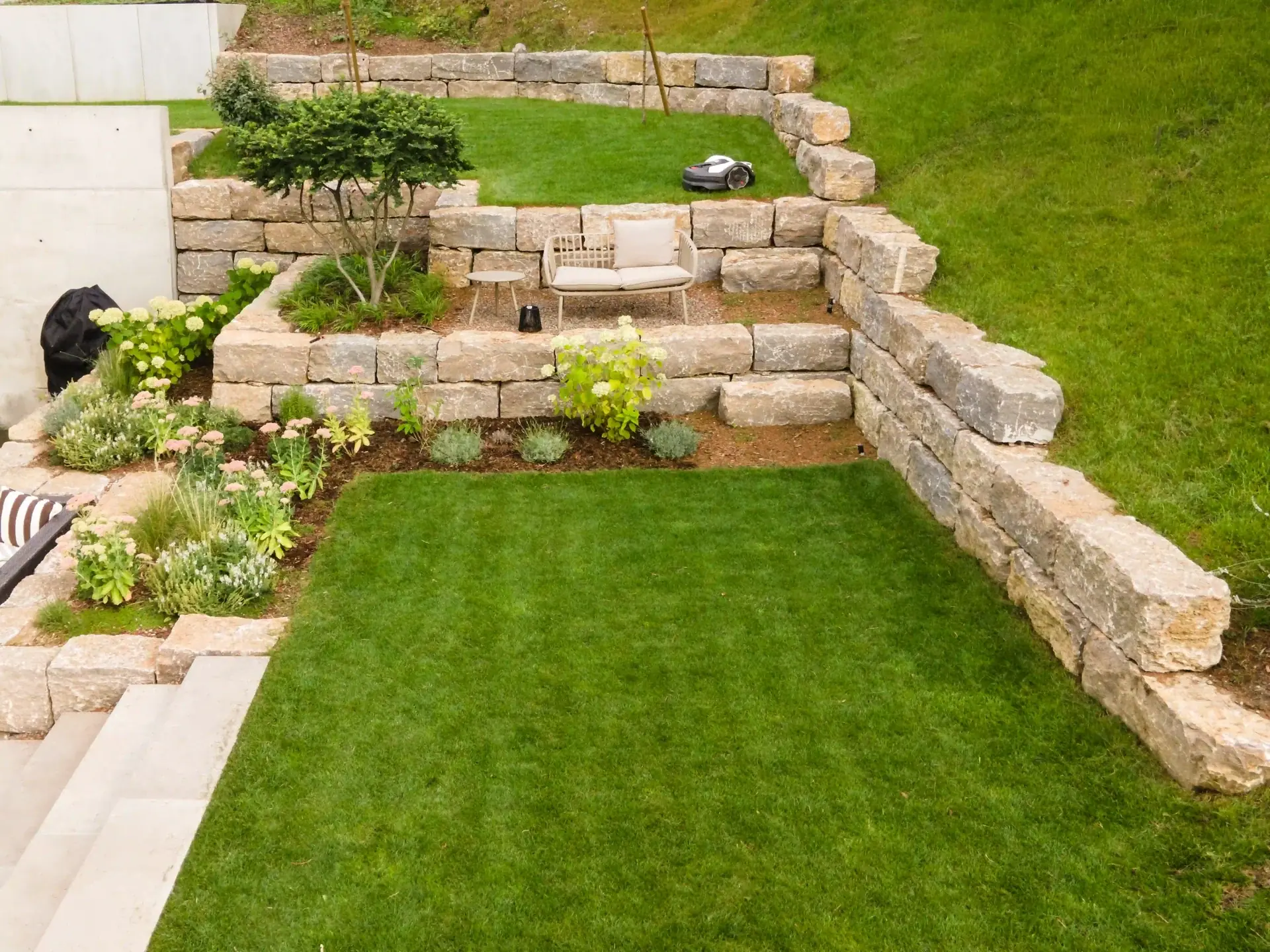 Garten mit Rasenfläche, Natursteinmauer und neu angelegten Beeten.