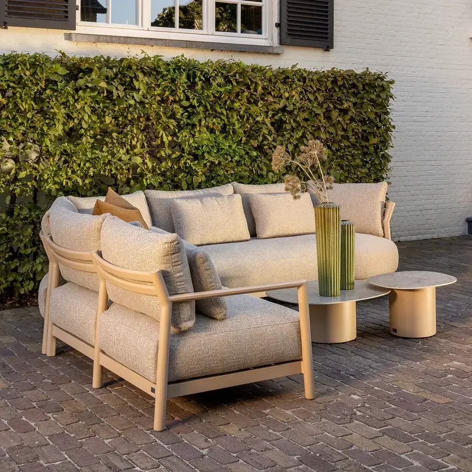 Helle Gartenlounge mit Sofa auf einem steinernen Terrassenboden.