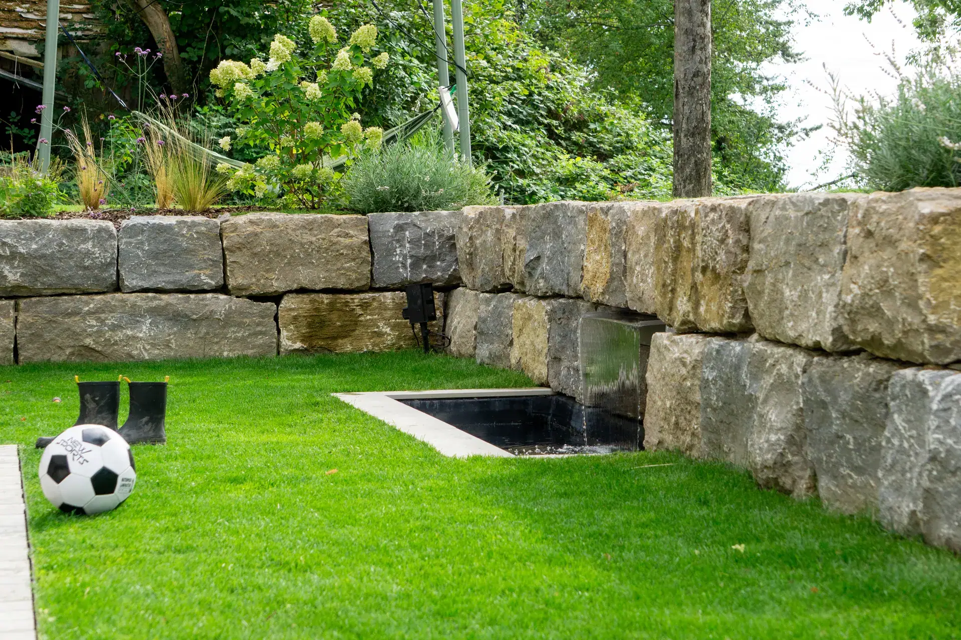 Natursteinmauer mit Rasen und kleinem Wasserbecken.