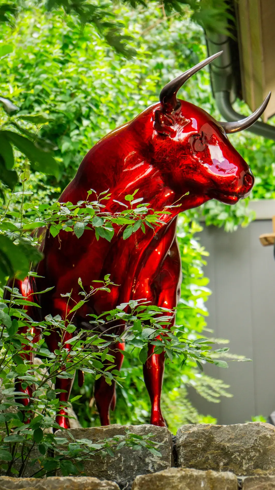 Rote Gartenskulptur zwischen Pflanzen.