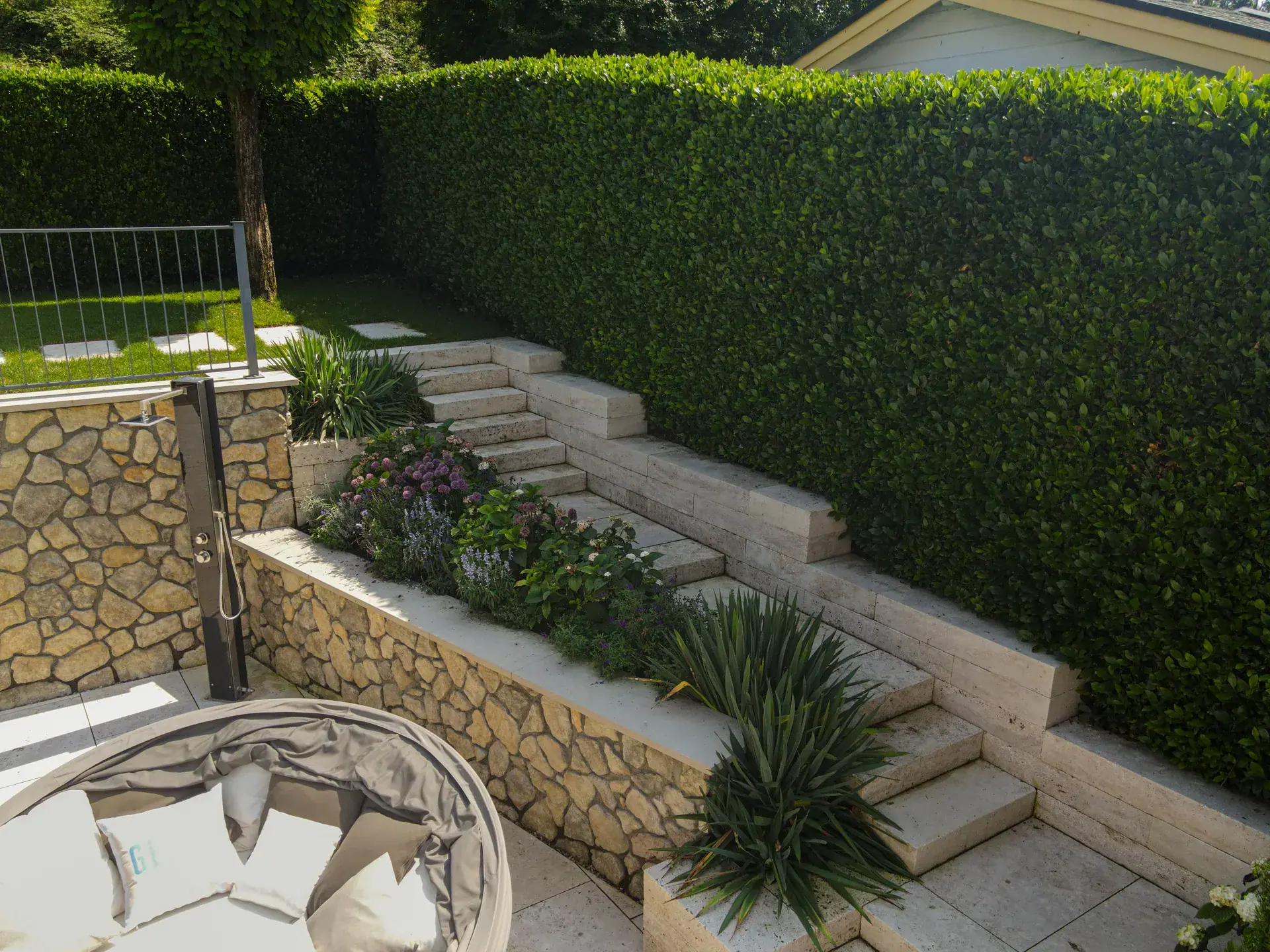 Steintreppe zwischen Natursteinmauer und dichter Hecke.