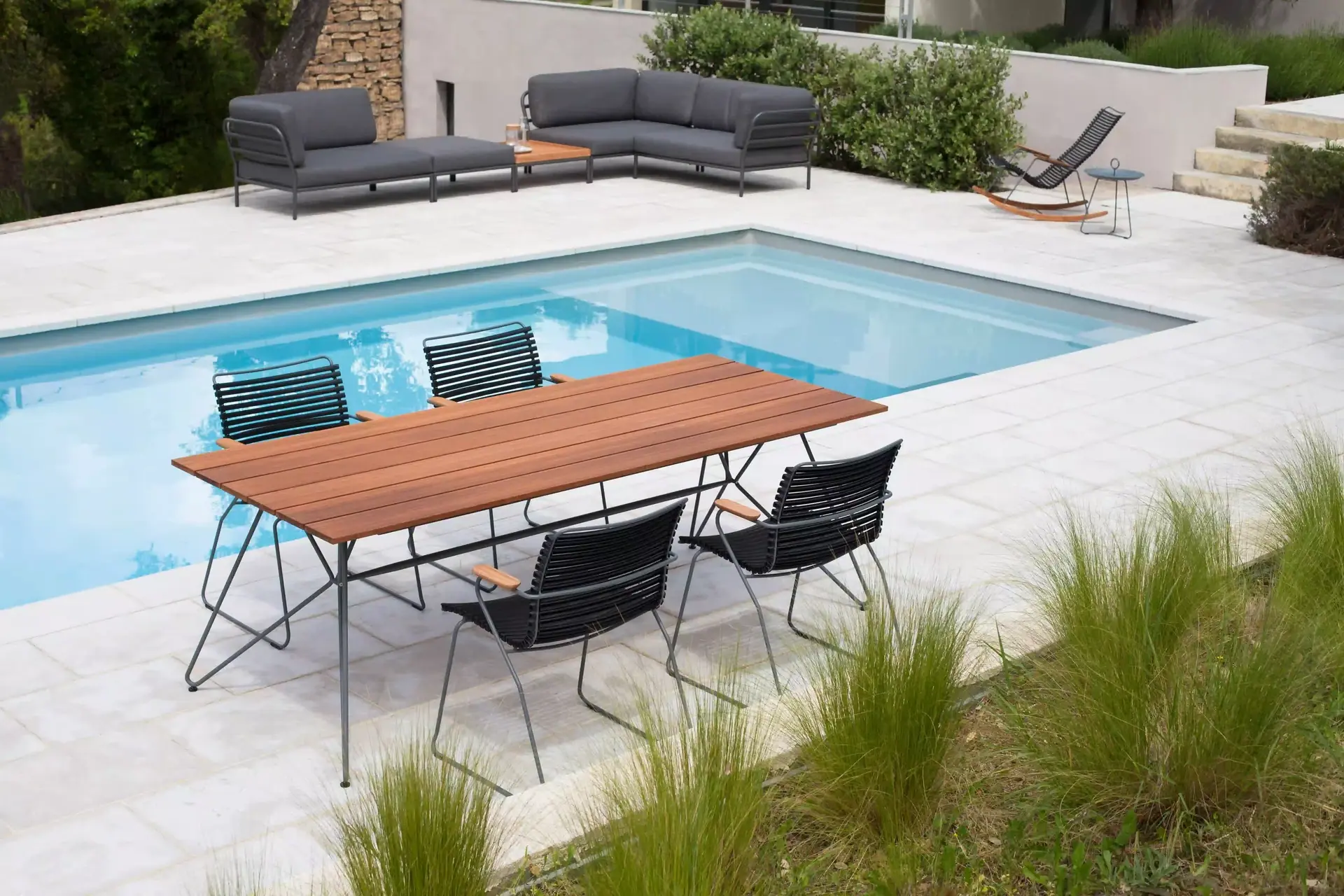Großer Gartentisch mit Stühlen auf einer Poolterrasse.