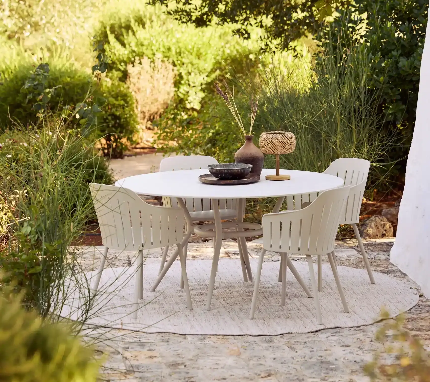 Runder Gartentisch mit hellen Stühlen auf einer Terrasse.