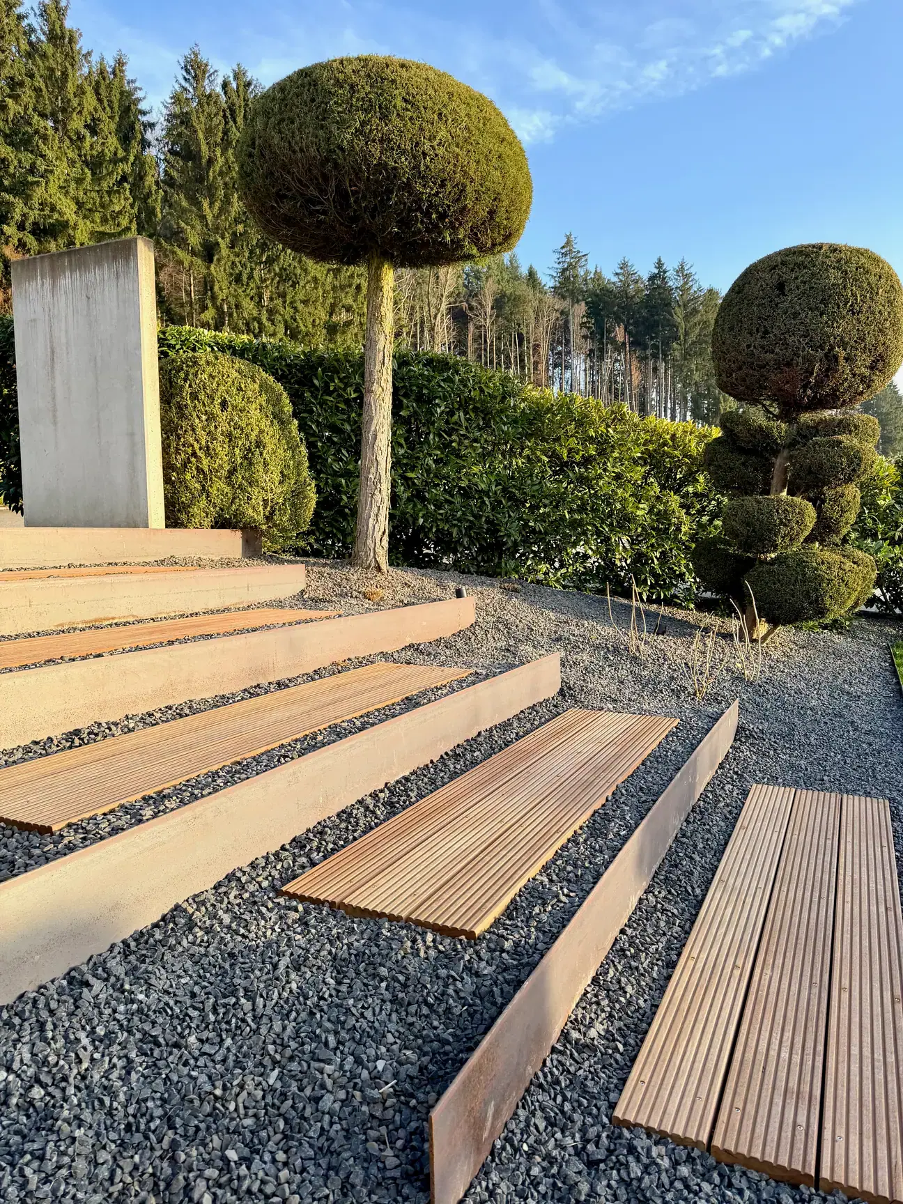 Gartenstufen mit Kugelbäumen und Kiesflächen.