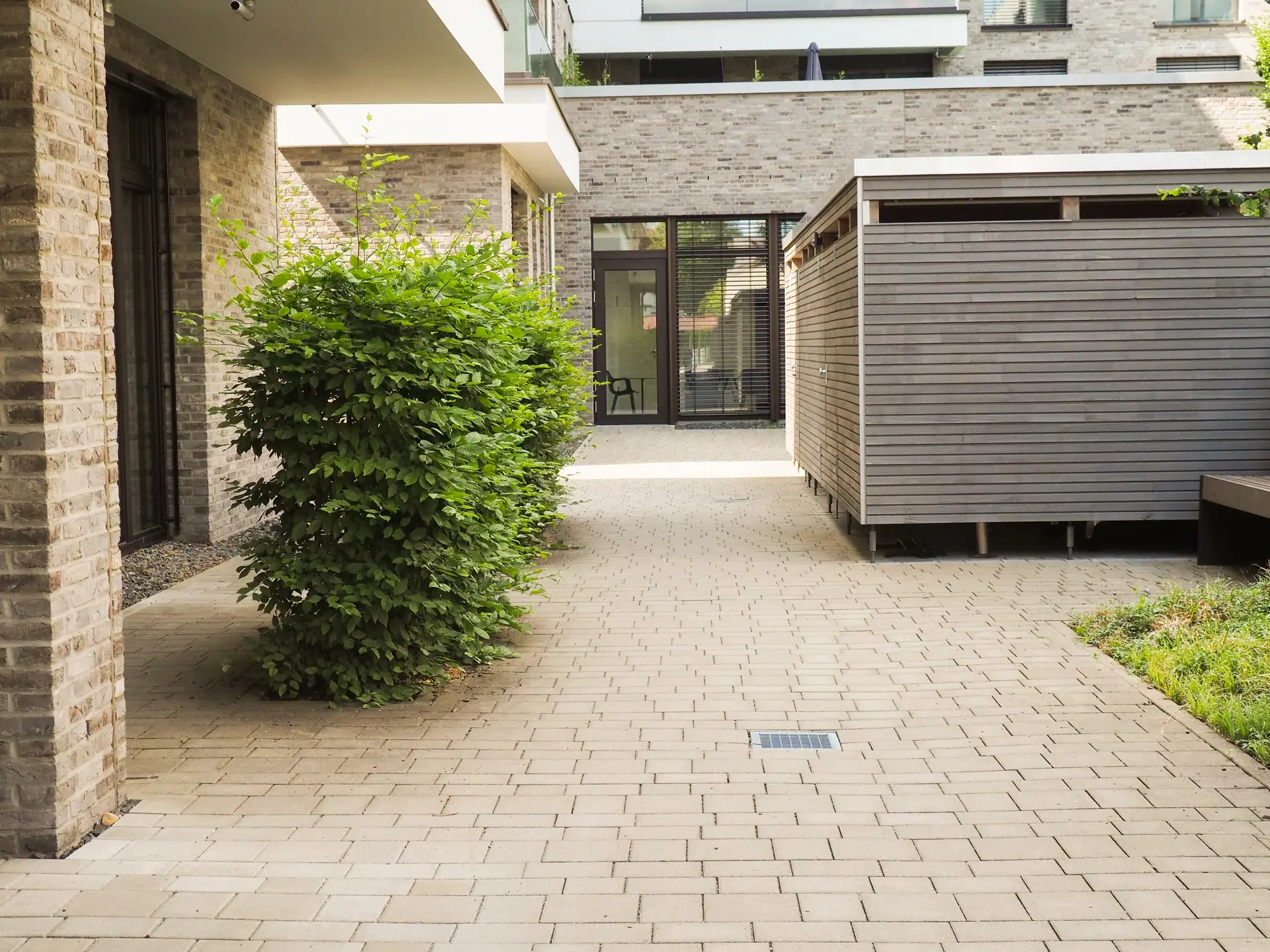 Gepflasterte Einfahrt zwischen bepflanzten Gebäuden.