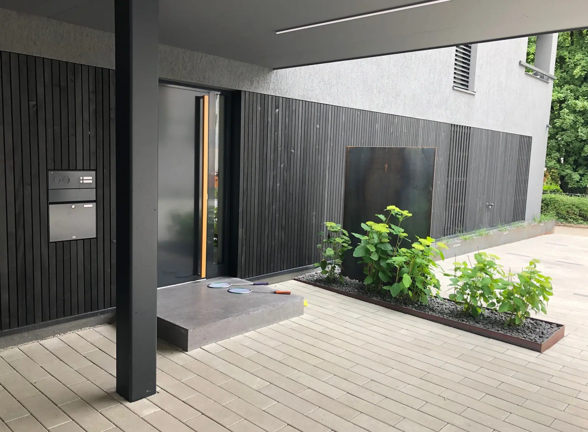 Eingangsbereich eines modernen Gebäudes mit Holzdeck und Pflanzbeet.