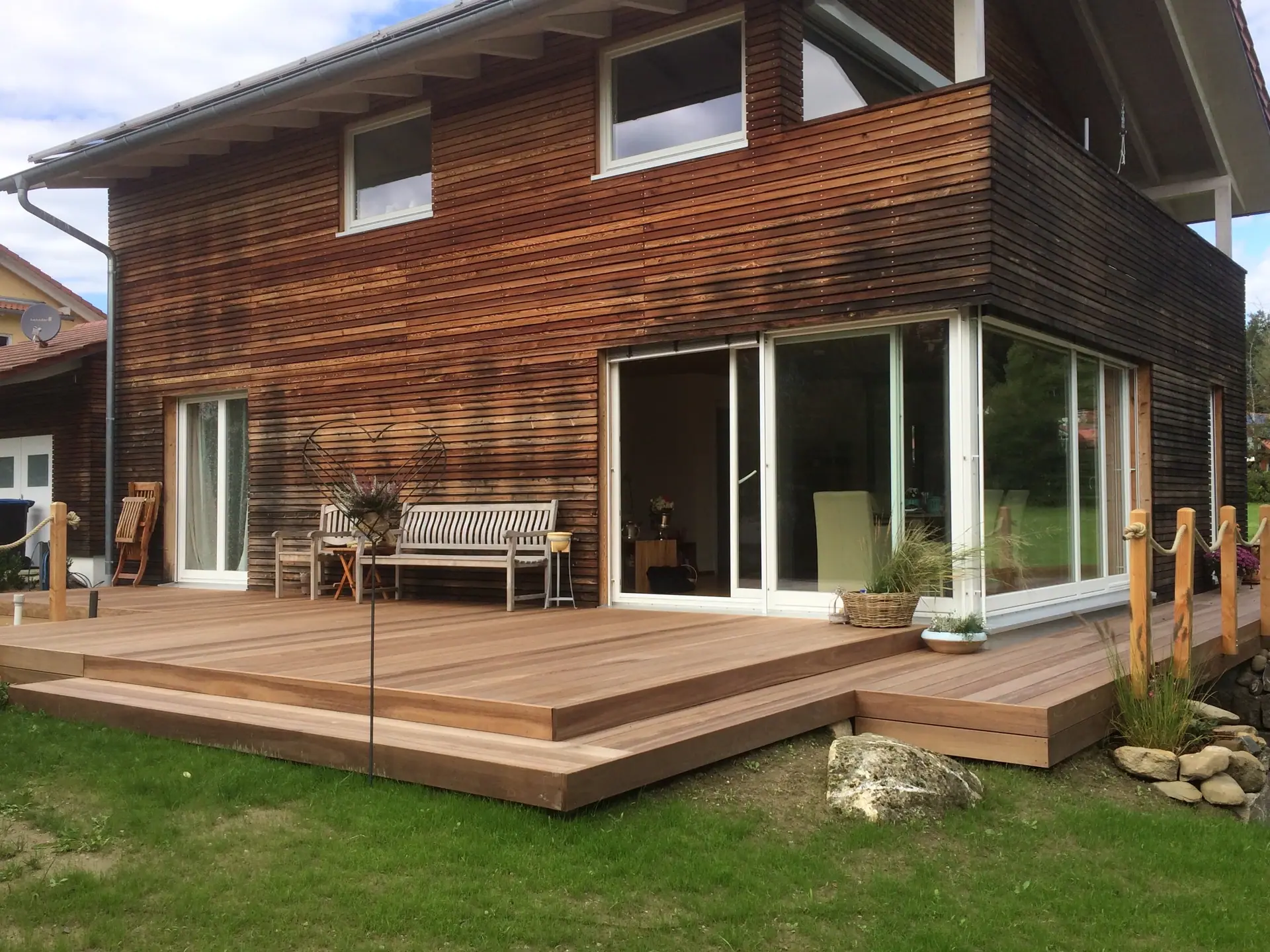 Holzterrasse mit Sitzbank vor einem Haus mit Holzfassade.