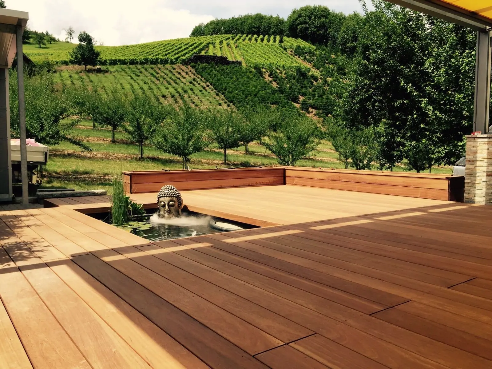 Großes Holzdeck mit Wasserspiel und Blick auf eine Wiese.