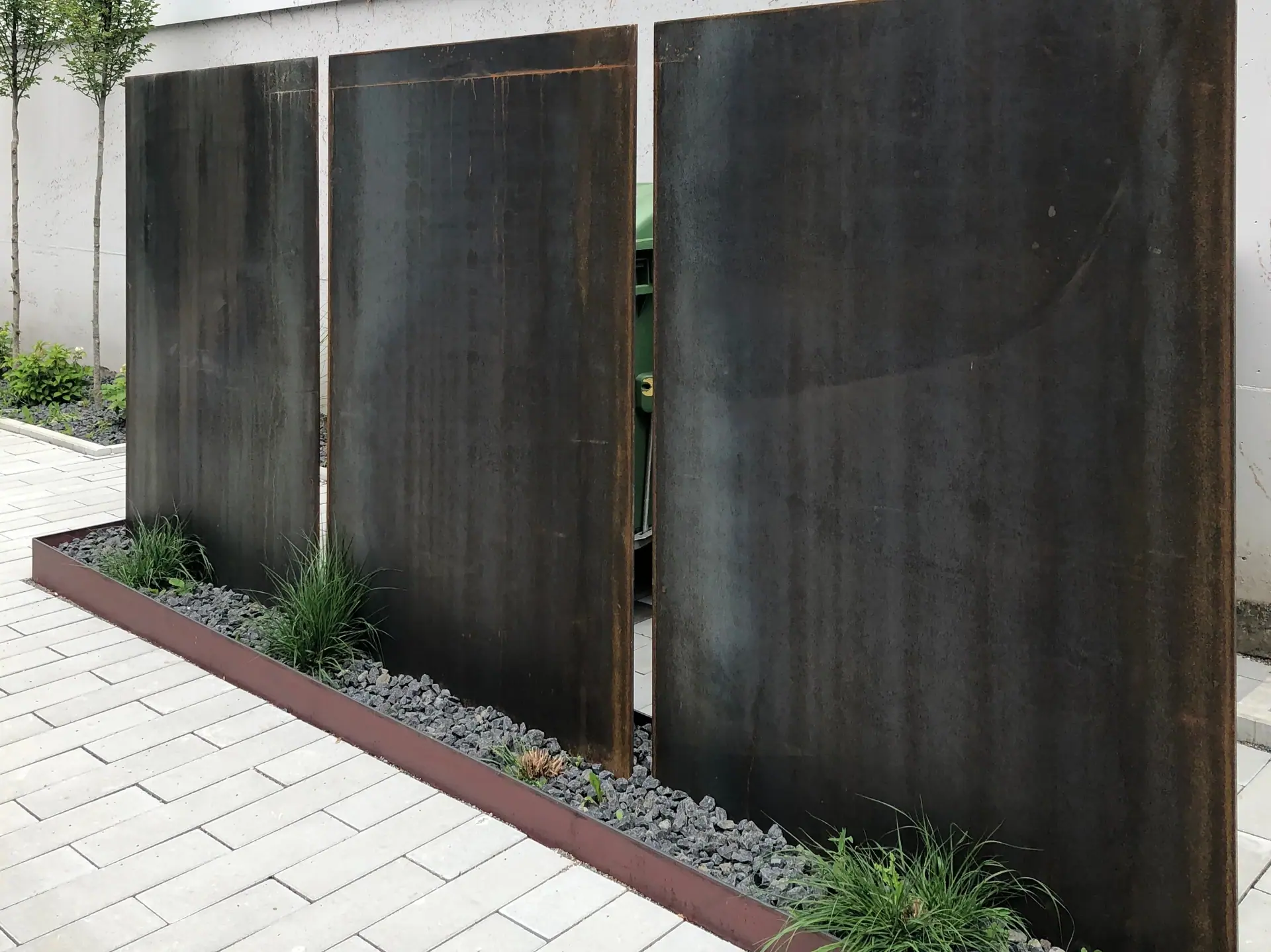 Dunkle Sichtschutzwand aus Metall an einem gepflasterten Weg.