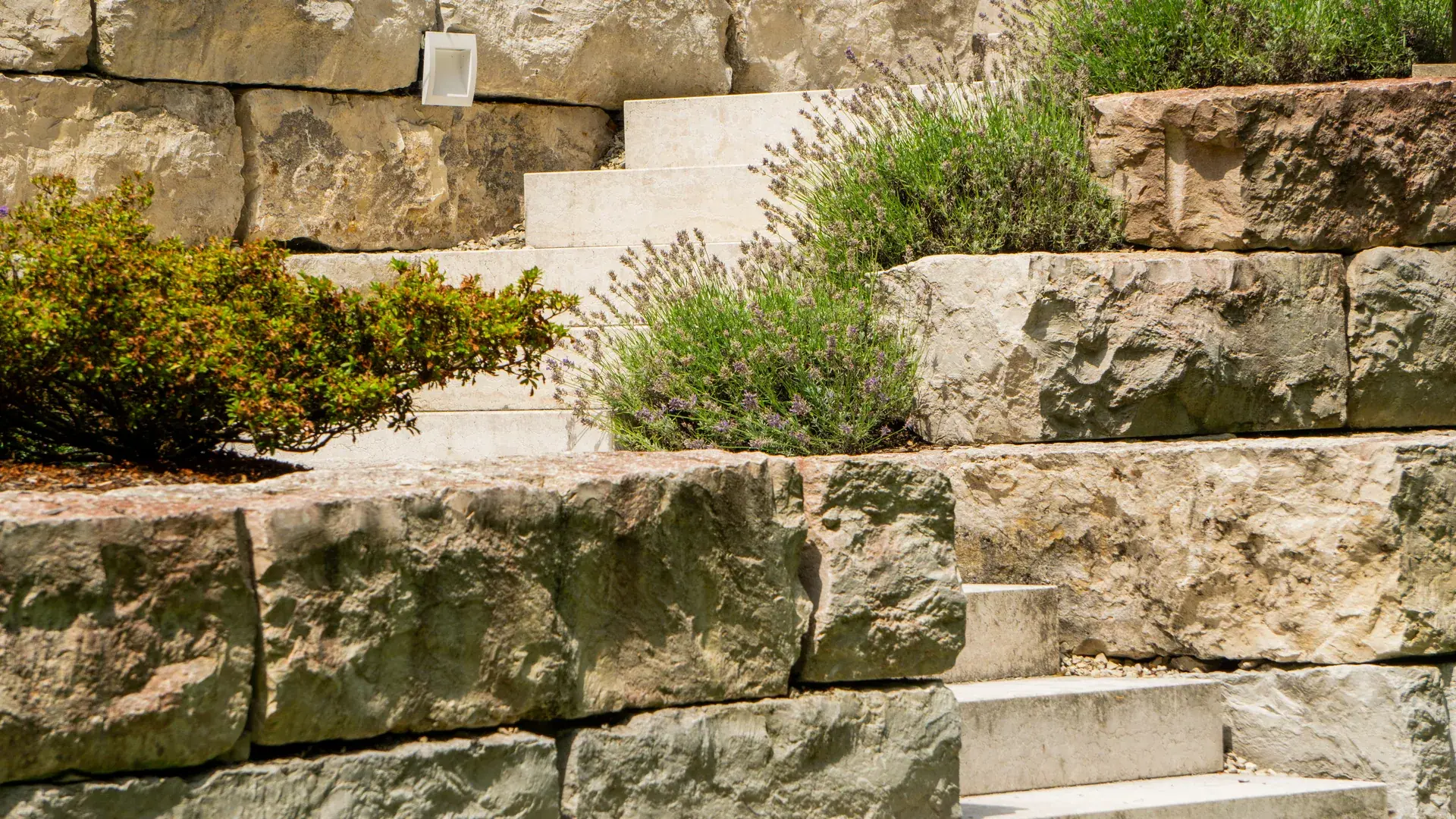 Natursteinmauer mit Pflanzbeeten und integrierter Treppe.