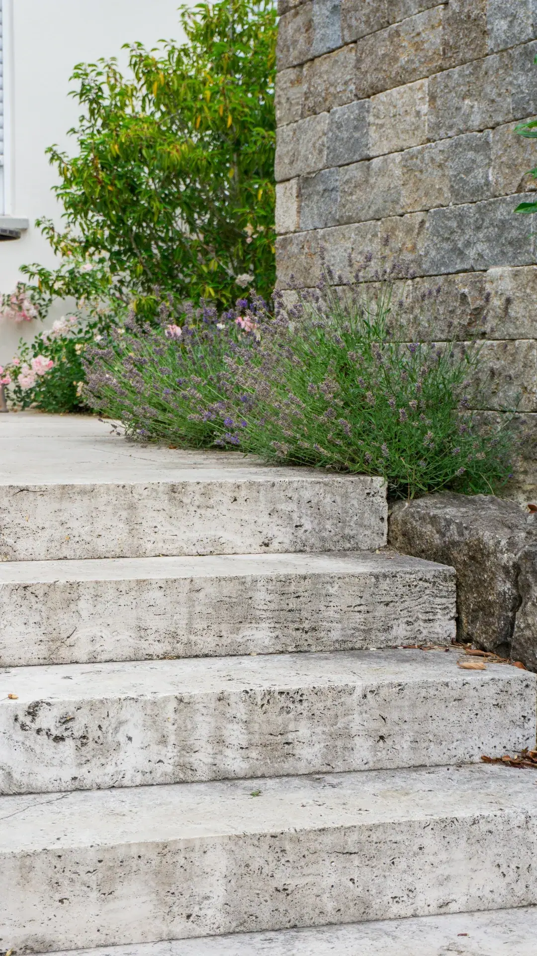 Breite Natursteintreppe zwischen einer Mauer und blühenden Stauden.