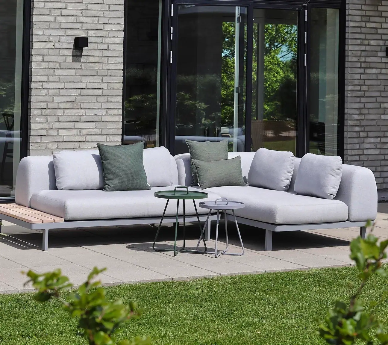 Helles Ecksofa auf einer Terrasse vor einem Haus.