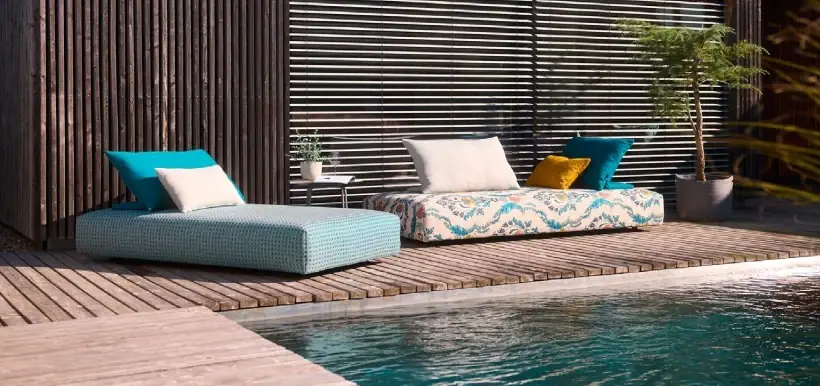 Outdoorsofa mit bunten Kissen auf einem Holzdeck am Pool.