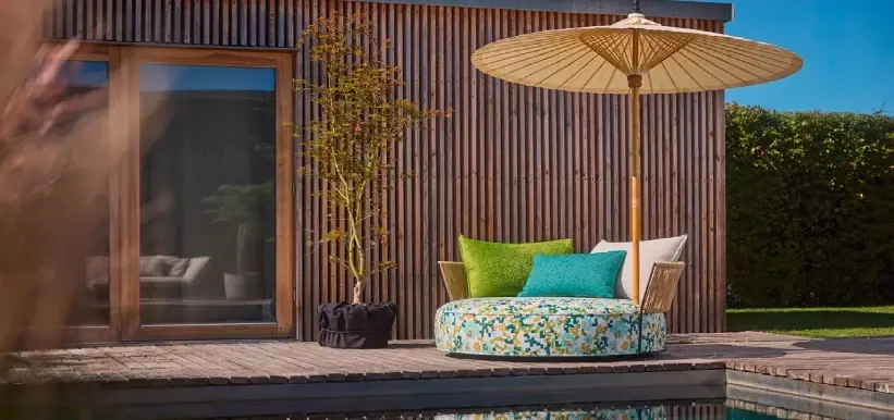 Buntes Outdoorsofa vor einer Holzfassade mit Sonnenschirm.
