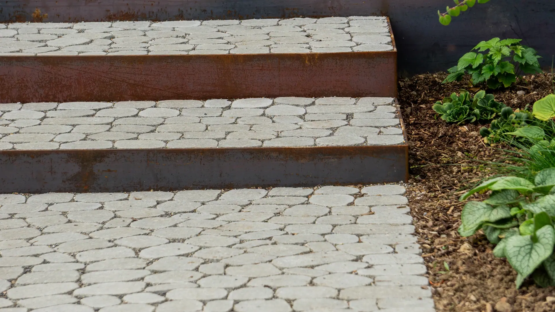 Pflasterweg mit drei breiten Stufen und Stahlkanten.