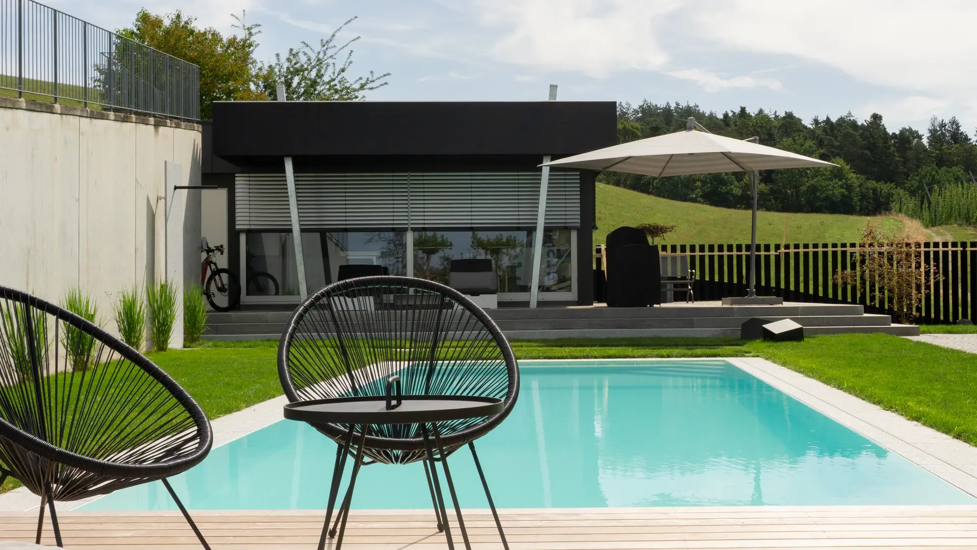 Pool mit Sitzmöbeln und Gartenhaus im Hintergrund.