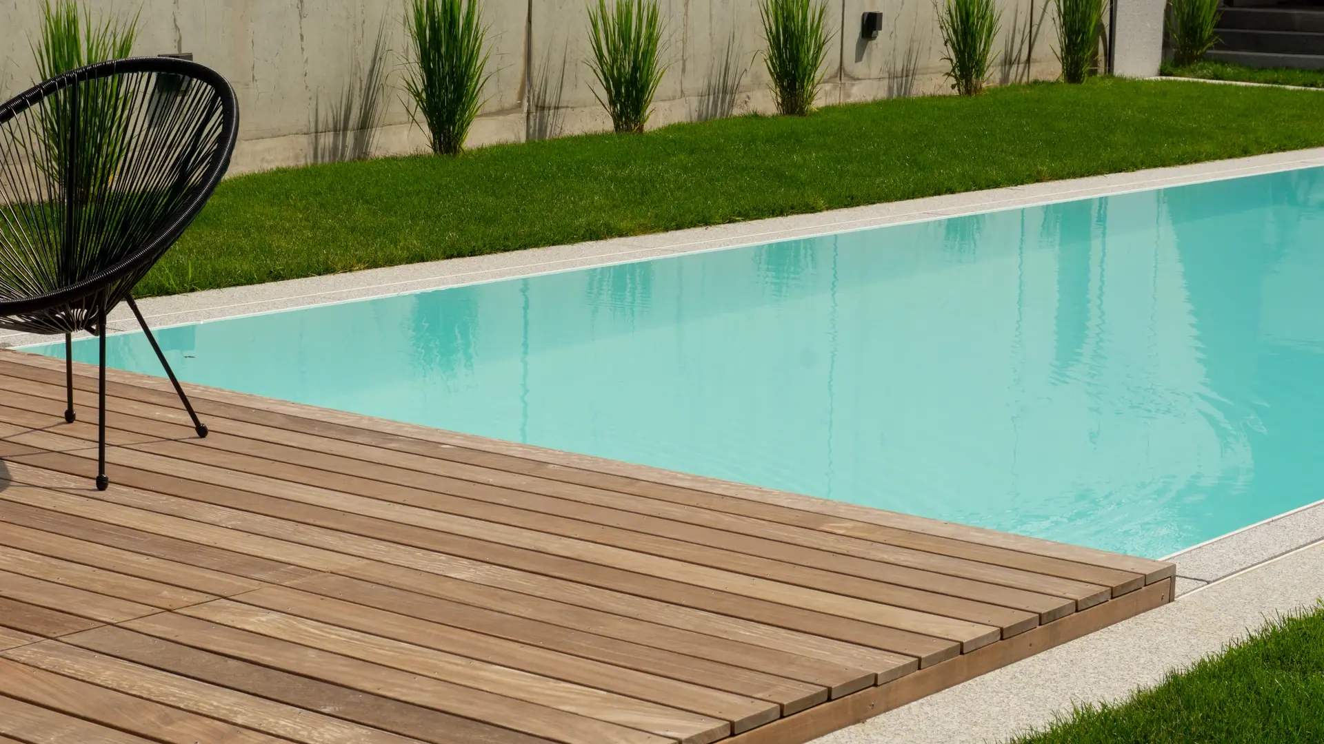 Pool mit Holzdeck und zwei dunklen Gartenstühlen.