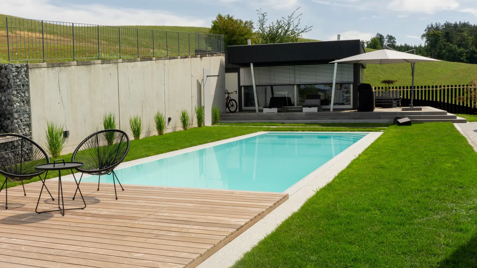 Pool mit Holzterrasse, Gartenstühlen und Gartenhaus.