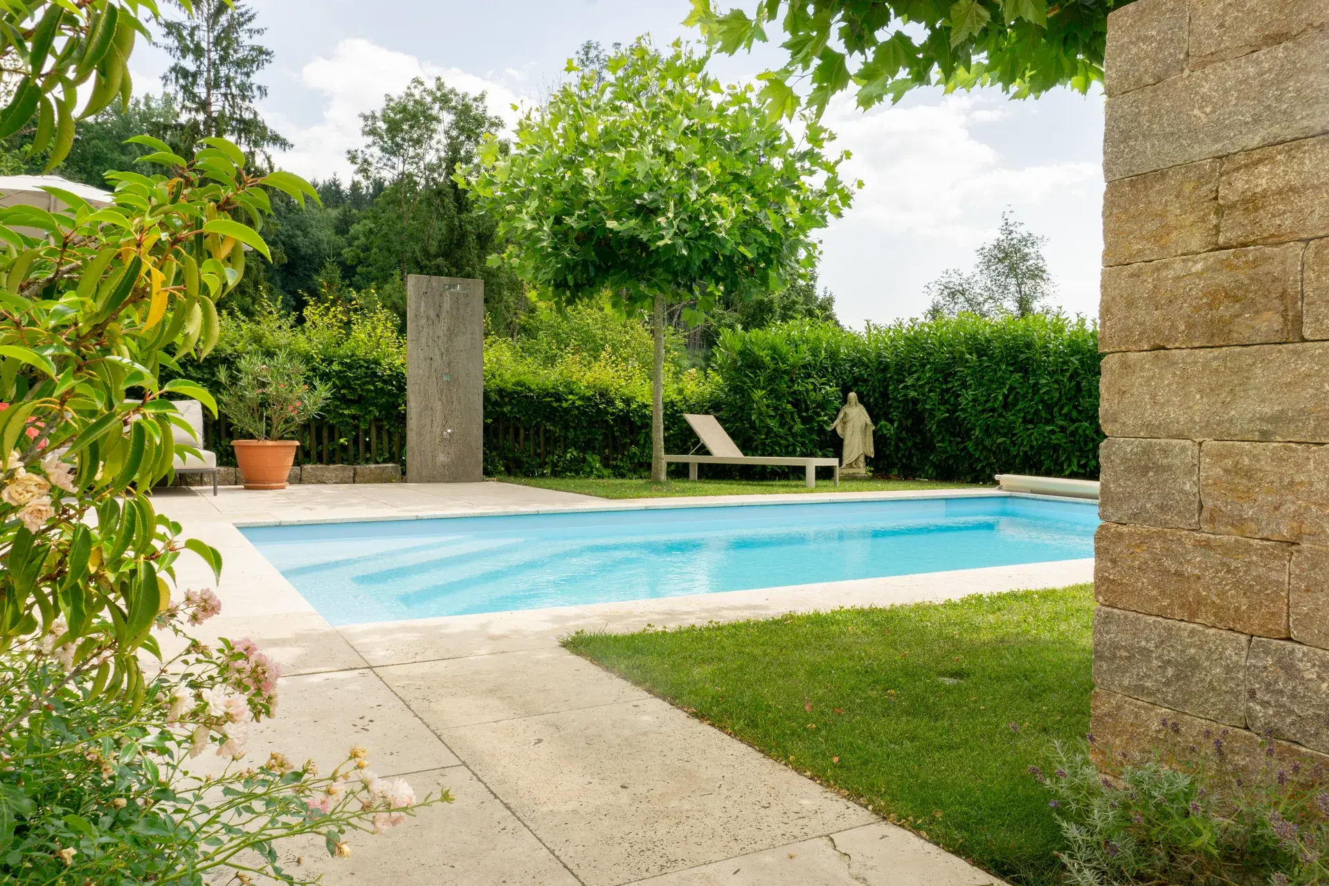 Pool mit Natursteinplatten und Bepflanzung.