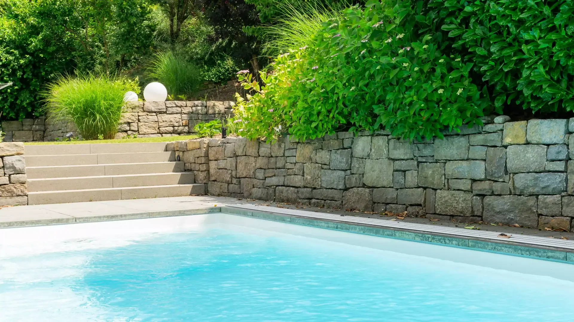 Pool vor einer Natursteinmauer und breiter Treppe.