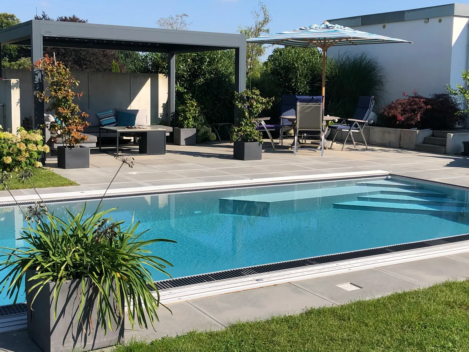 Pool mit Gartenlounge unter einer Pergola.