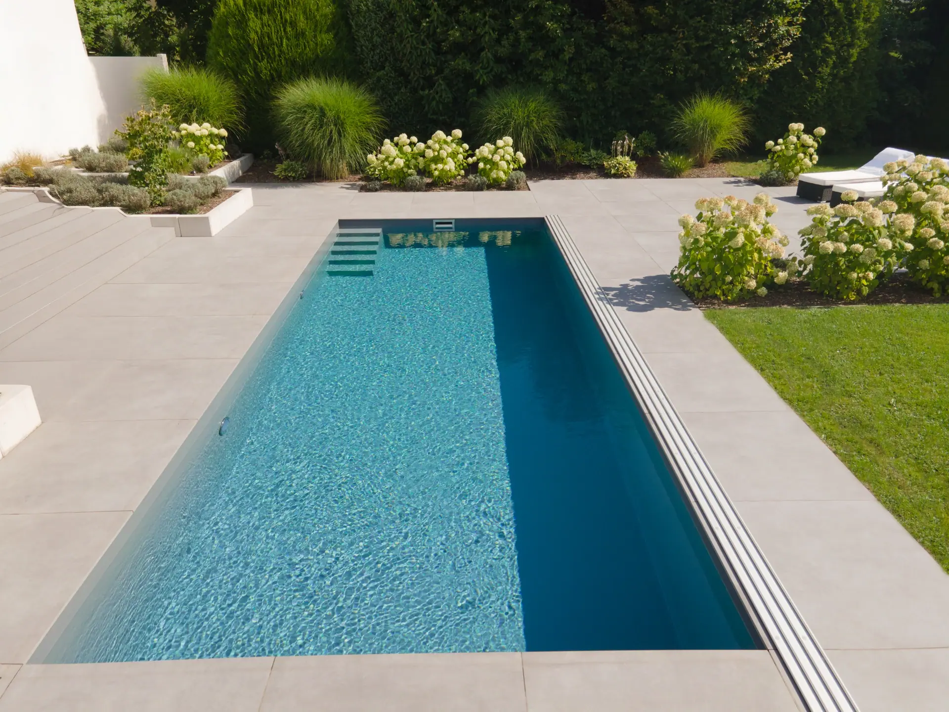 Schmaler Pool zwischen Terrasse und Rasenfläche.