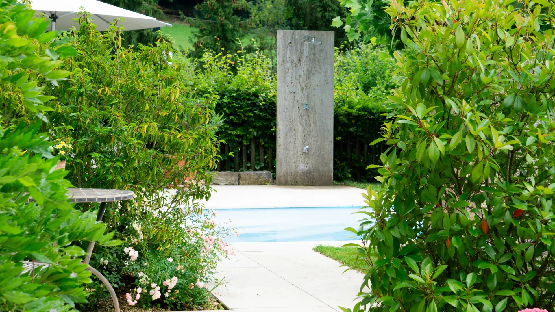 Pool mit Steinpfeiler hinter dichter Bepflanzung.