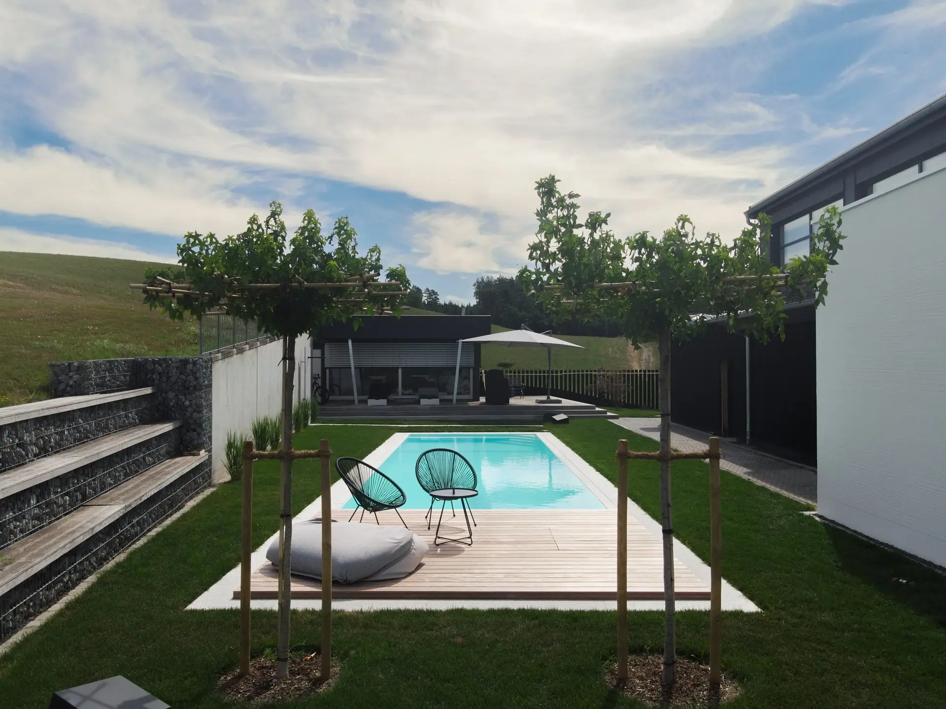 Gesamtansicht eines Gartens mit Pool, Holzdeck und Sitzplatz.