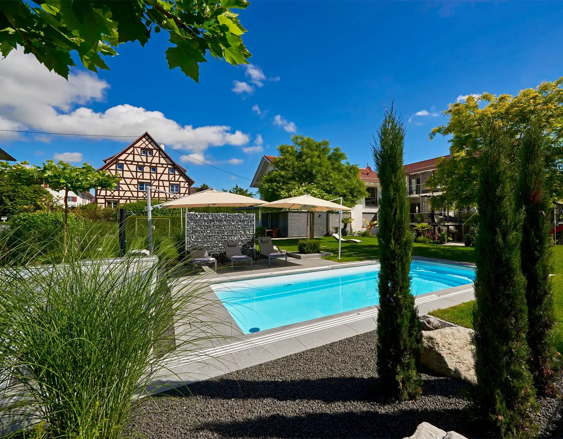 Poolgarten mit Zypressen und Haus im Hintergrund.