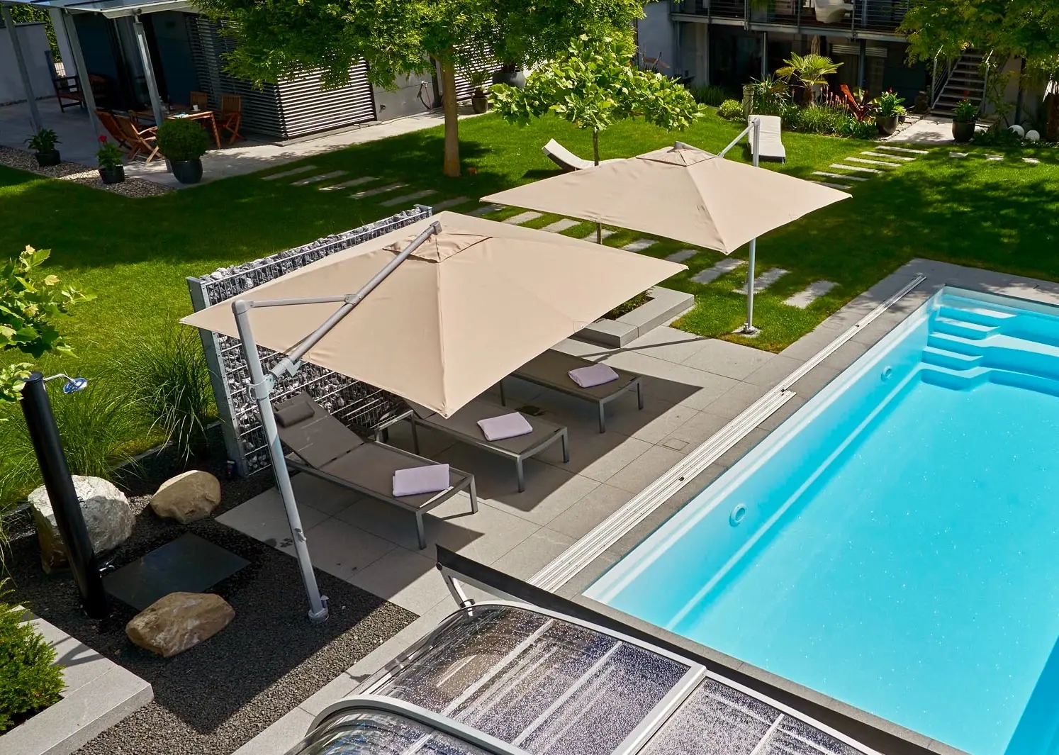 Poolterrasse mit Liegen und mehreren Sonnenschirmen.