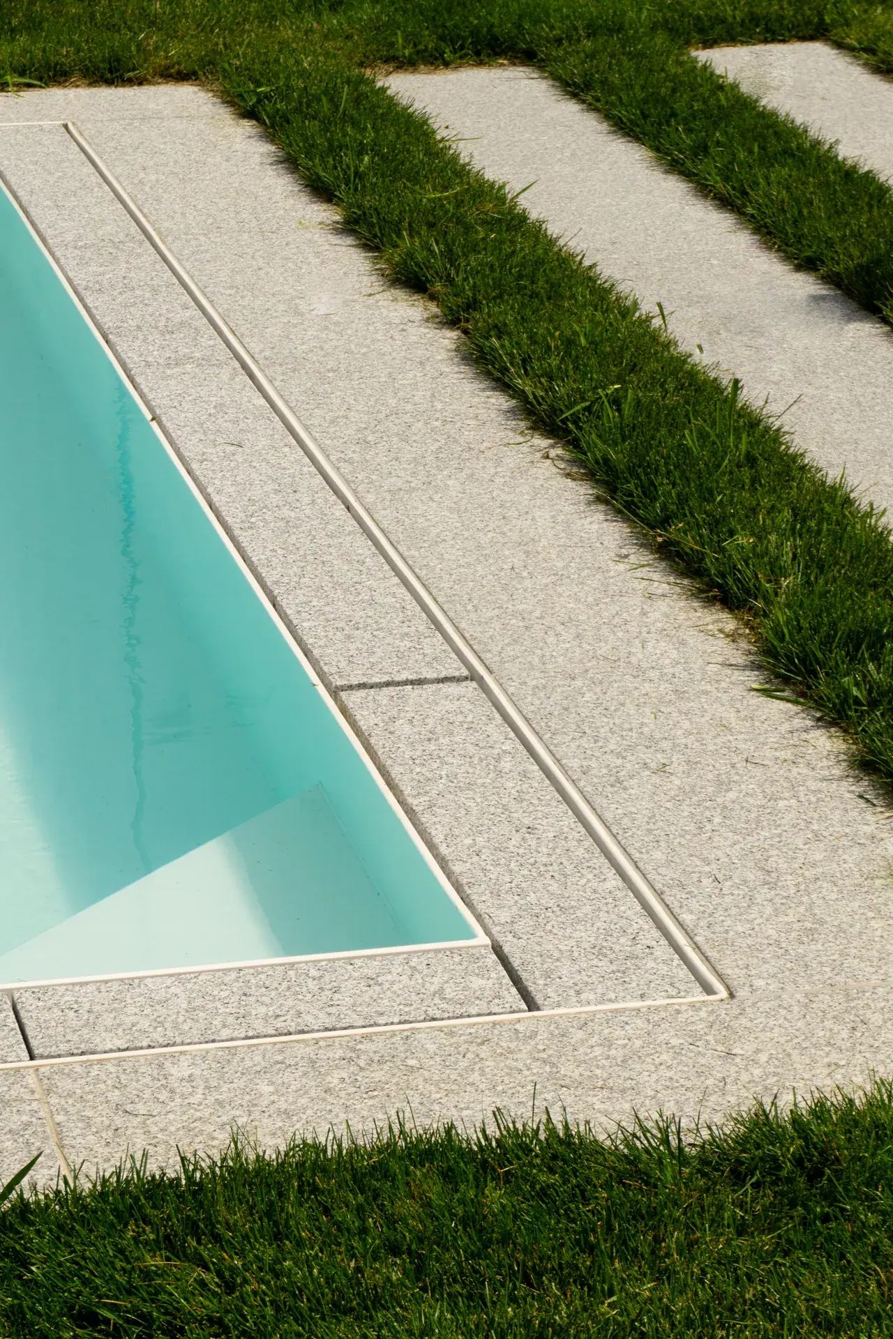 Poolrand mit Natursteinplatten und Rasenfugen.