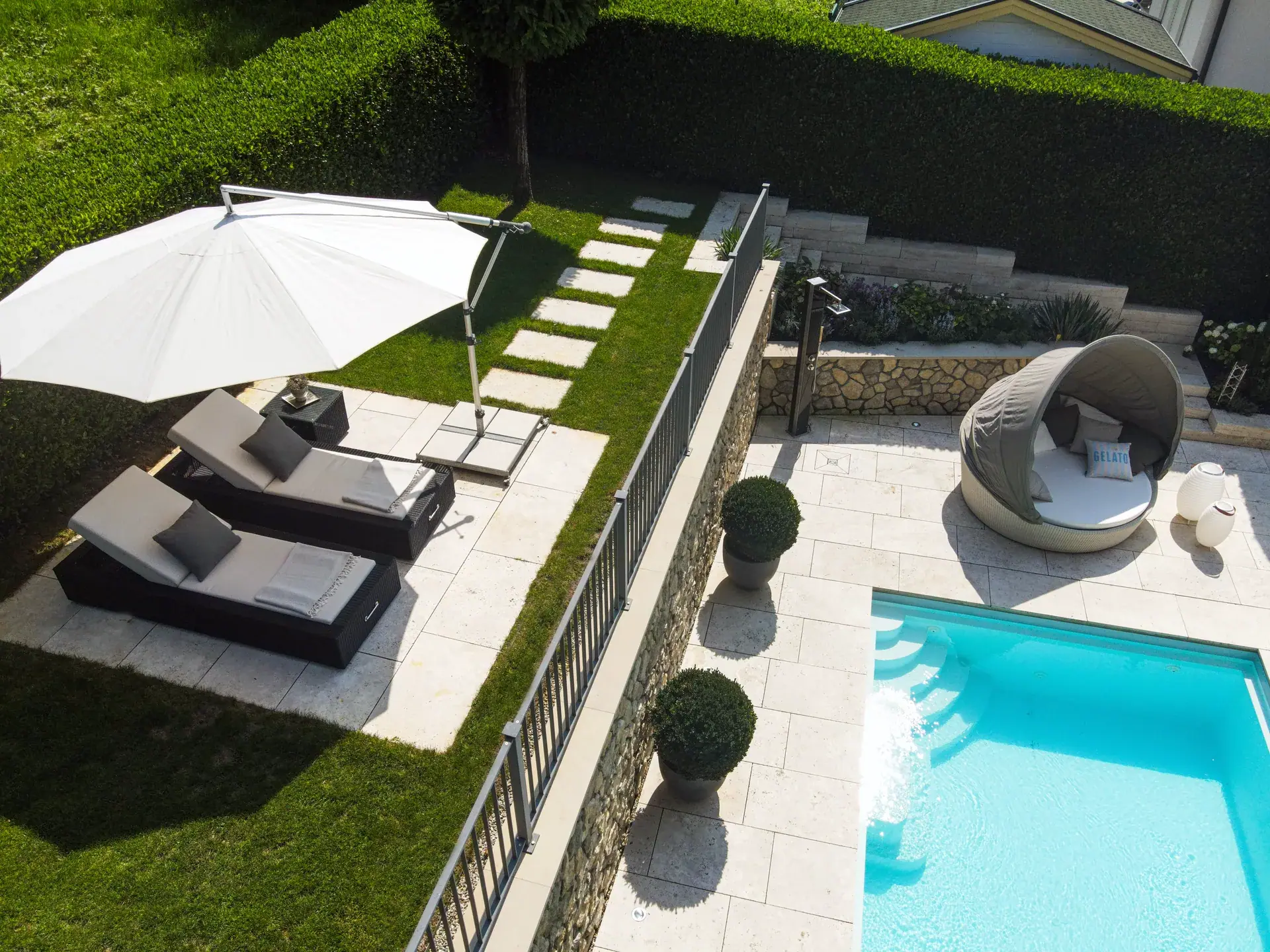Luftaufnahme von Poolterrasse, Liegen und Gartenwegen.