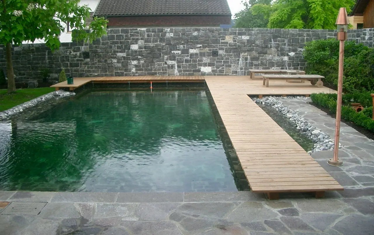 Schwimmteich mit Holzsteg und Natursteinbelag.