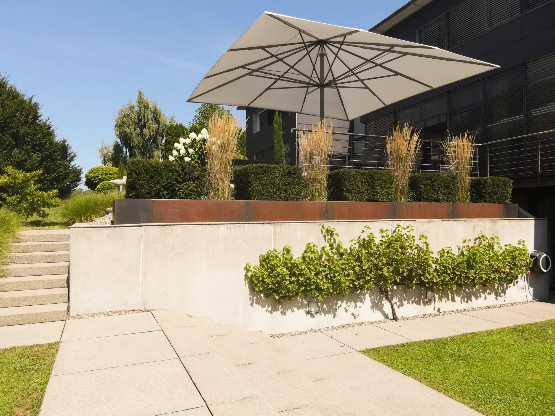 Erhöhte Terrasse mit Sonnenschirm und Pflanzbeeten.