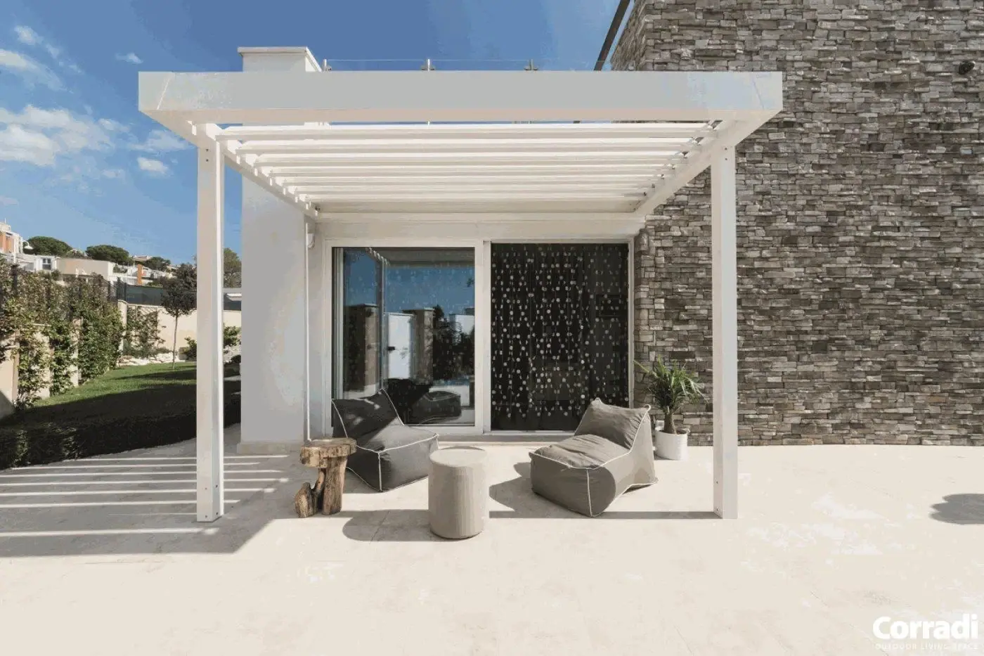 Weiße Terrassenüberdachung mit Sitzmöbeln vor einer Steinwand.